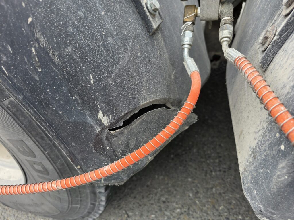 Other brand thermoformed plastic mudguard showing tear and cracking near edge in service