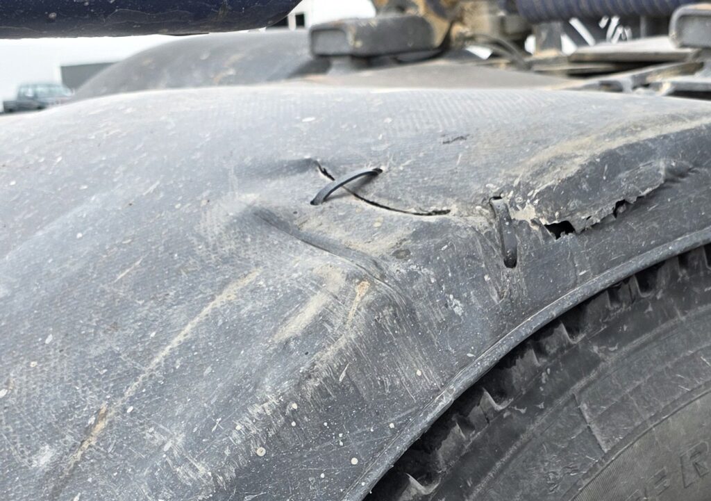 Other brand thermoformed plastic mudguard showing tearing and cracking with cable tie repair in service